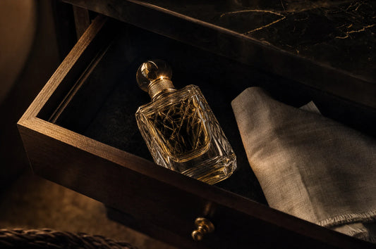 Flakon perfum w otwartej ciemnej szufladzie wyłożonej czarnym weluerem, obok złożona lniana ściereczka